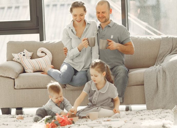 Cheerful family wearing casual clothes sitting in living room while playing and drinking tea during weekend at home in morning