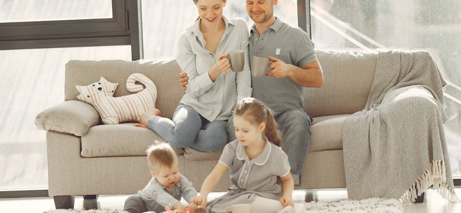 Cheerful family wearing casual clothes sitting in living room while playing and drinking tea during weekend at home in morning